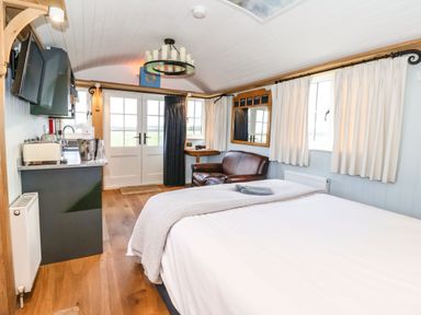 A bedroom with a bed leather chair kitchenette and double doors at The Fenton in Bolton Percy near Tadcaster