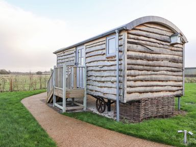 A wooden shepherd hut with steps leading to a door on a gravel path in a grassy field at The Fenton in Bolton Percy near Tadcaster