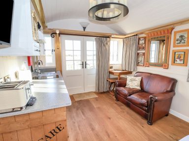 A kitchen and sitting area with a brown leather sofa and a small table near French doors at The Egyptologist in Bolton Percy near Tadcaster