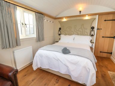 A bedroom with a bed with white bedding and a gray throw blanket under windows with striped curtains at The Egyptologist in Bolton Percy near Tadcaster