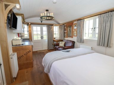 A bedroom with a bed a brown leather armchair a small wooden desk kitchen cabinets and double doors leading outside at The Egyptologist in Bolton Percy near Tadcaster