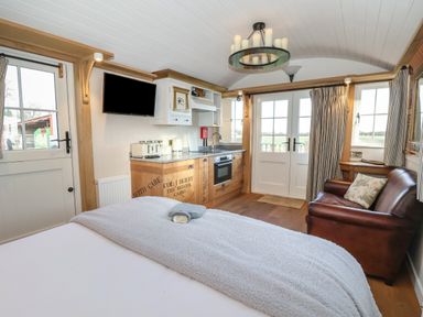 A small kitchen area with oven and sink next to a leather sofa and bed in a room with windows and doors at The Egyptologist in Bolton Percy near Tadcaster
