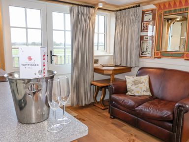 A room with a brown leather sofa next to a corner wooden table and two champagne glasses with a champagne bottle in an ice bucket on a countertop at The Studio in Bolton Percy near Tadcaster