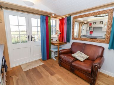 A room with a brown leather sofa colorful curtains a wooden desk with a lamp and double glass doors at The Studio in Bolton Percy near Tadcaster