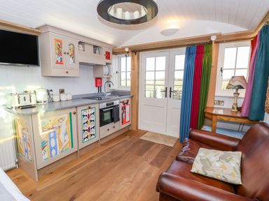 A kitchen area with painted cabinets and a brown leather sofa near a wooden table with a lamp at The Studio in Bolton Percy near Tadcaster