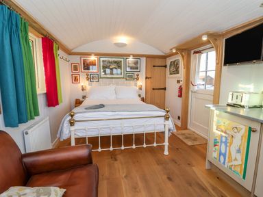 A bedroom with a white metal bed blue green and red curtains a leather armchair and a TV at The Studio in Bolton Percy near Tadcaster