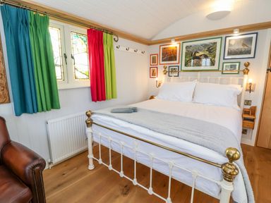 A bedroom with a white and brass bed beside colorful curtains and framed pictures on the wall at The Studio in Bolton Percy near Tadcaster