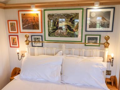 A bed with white pillows and an iron headboard with brass details below framed pictures on a white paneled wall at The Studio in Bolton Percy near Tadcaster