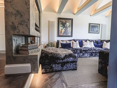 A living room with a sectional sofa with cushions a textured fireplace and framed wall art at Whisk Away Cottage Greystoke near Troutbeck Near Penrith
