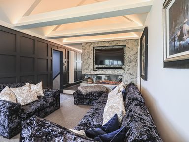 A living room with black velvet sofas and a wall-mounted TV above a modern fireplace at Whisk Away Cottage Greystoke near Troutbeck Near Penrith