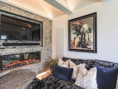 A living room with a mounted television above a fireplace a sofa with cushions and a framed painting on the wall at Whisk Away Cottage in Greystoke near Troutbeck Near Penrith
