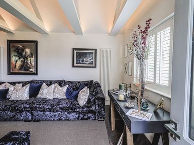 A living room with dark sofa and cushions next to a black table with decorative items and flowers at Whisk Away Cottage Greystoke near Troutbeck Near Penrith