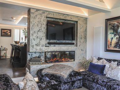 A living room with a wall-mounted television above a fireplace and a sectional sofa with cushions at Whisk Away Cottage in Greystoke near Troutbeck Near Penrith