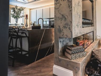 A kitchen with a black marble island and bar stools next to a fireplace with decorative books at Whisk Away Cottage in Greystoke near Troutbeck Near Penrith