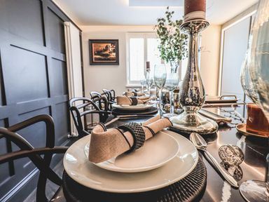 A dining table set with plates napkins cutlery glasses and a candlestick in a room with dark paneled walls and a window at Whisk Away Cottage in Greystoke near Troutbeck Near Penrith