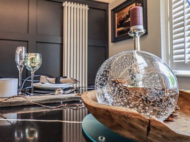 A dining table with glassware plates and napkins and a decorative glass bowl with pinecones at Whisk Away Cottage in Greystoke near Troutbeck Near Penrith