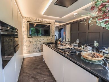 A modern kitchen with a black countertop island dining setup and a wall-mounted television at Whisk Away Cottage Greystoke near Troutbeck Near Penrith