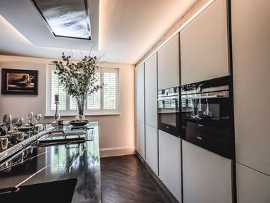 A modern kitchen with built-in ovens, a marble countertop with glasses and a vase of flowers by a window at Whisk Away Cottage in Greystoke near Troutbeck Near Penrith