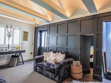 A living room with a dark sofa with cushions a console table with decor and a basket with blankets at Whisk Away Cottage in Greystoke near Troutbeck Near Penrith