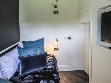 A bedroom corner with a bed with multiple pillows and a mounted television at Whisk Away Cottage Greystoke near Troutbeck Near Penrith