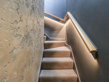 A stairway with carpeted steps and wooden handrails on textured and smooth walls at Whisk Away Cottage Greystoke near Troutbeck Near Penrith