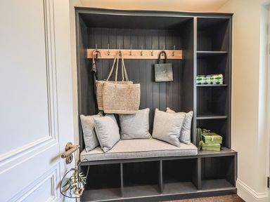 A built-in bench with cushions hooks holding bags and umbrella and shelving with boxes at Whisk Away Cottage Greystoke near Troutbeck Near Penrith