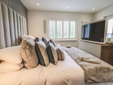 A bedroom with a bed with multiple pillows and a television on a dresser at Whisk Away Cottage in Greystoke near Troutbeck Near Penrith