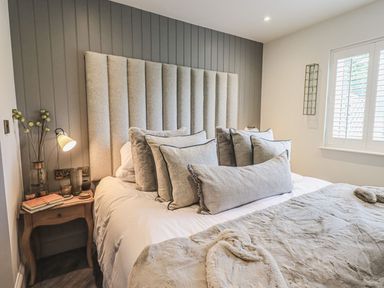 A bedroom with a bed with multiple pillows and a bedside table with books and a lamp at Whisk Away Cottage in Greystoke near Troutbeck Near Penrith