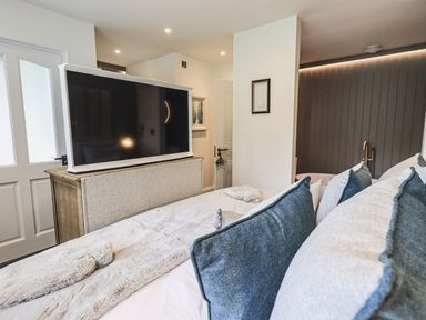 A bedroom with a bed with pillows and a blanket a television on a stand a door and framed pictures on the wall at Whisk Away Cottage Greystoke near Troutbeck Near Penrith