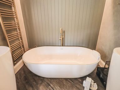 A bathroom with a freestanding bathtub a towel rack and toiletries on the floor at Whisk Away Cottage Greystoke near Troutbeck Near Penrith