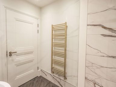 A wall-mounted towel radiator next to a closed white door in a bathroom with marble wall tiles at Whisk Away Cottage in Greystoke near Troutbeck Near Penrith