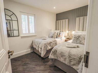 A bedroom with two single beds side by side with headboards a window with shutters and a wall mirror at Whisk Away Cottage in Greystoke near Troutbeck Near Penrith