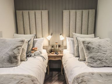 A bedroom with two beds side by side with a shared wooden nightstand and wall lamps at Whisk Away Cottage in Greystoke near Troutbeck Near Penrith