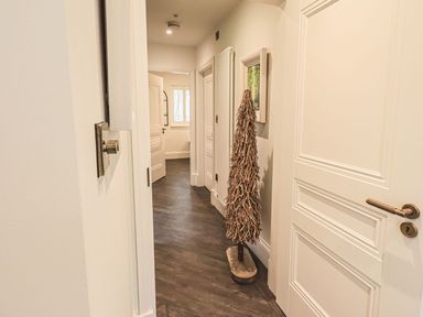A hallway with white doors wood floor a decorative wooden sculpture and a framed picture on the wall at Whisk Away Cottage in Greystoke near Troutbeck Near Penrith