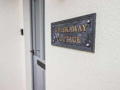 A door with a metal nameplate that reads Whiskaway Cottage on a white wall at Whisk Away Cottage in Greystoke near Troutbeck Near Penrith