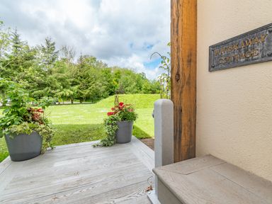 An outdoor wooden porch with potted plants and a sign reading Whiskaway Cottage at Whisk Away Cottage Greystoke near Troutbeck Near Penrith