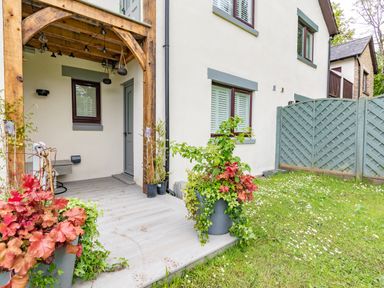 An outdoor area with a wooden porch structure plants in pots on wooden decking and a garden with a fence at Whisk Away Cottage in Greystoke near Troutbeck Near Penrith