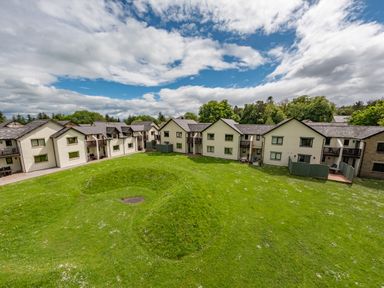 A group of two-story residential buildings with balconies and a large green lawn under a partly cloudy sky at Whisk Away Cottage Greystoke near Troutbeck Near Penrith