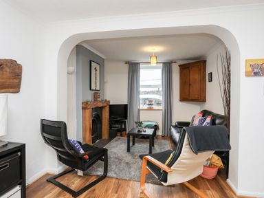 A living room with black chairs a wooden floor a fireplace and a small table at 5 Thomas Street in Llanberis