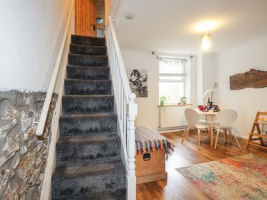 A carpeted staircase leading to a wooden door with a dining area to the right including a table with four chairs and a wooden chest covered with a striped blanket at 5 Thomas Street in Llanberis