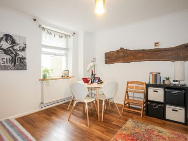 A dining area with a round table and four chairs next to a window with blinds and a cabinet with storage boxes at 5 Thomas Street in Llanberis