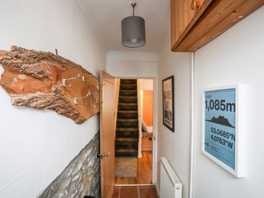 A hallway with a wooden coat rack with metal hooks a door leading to carpeted stairs and framed artwork on the walls at 5 Thomas Street in Llanberis