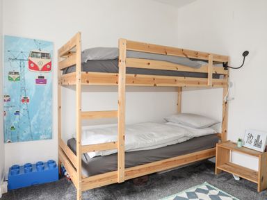 A bedroom with a wooden bunk bed a small wooden shelf a painting on the wall and a blue storage box at 5 Thomas Street in Llanberis