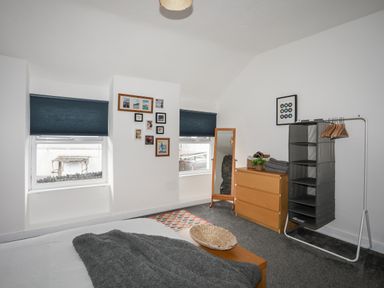 A bedroom with two windows two framed photo collages a standing mirror a wooden dresser and an open wardrobe at 5 Thomas Street in Llanberis