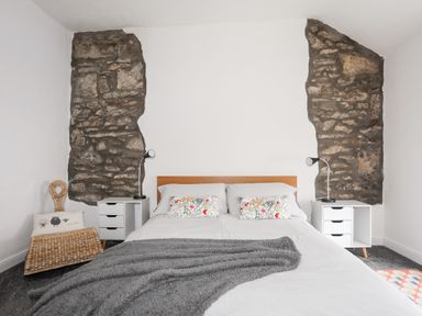 A bedroom with a bed between two stone wall sections and bedside tables with lamps at 5 Thomas Street in Llanberis