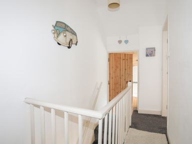 A hallway with white walls, a wooden door, a stair railing, and a decorative van wall hanging at 5 Thomas Street in Llanberis