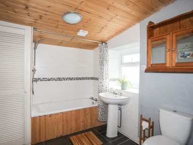 A bathroom with a bathtub shower combination a pedestal sink a wooden cabinet and a toilet at 5 Thomas Street in Llanberis