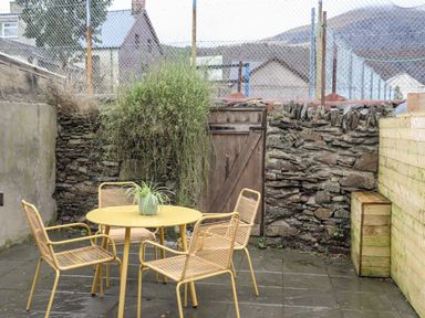 An outdoor patio with a yellow round table surrounded by four matching chairs and a small plant on the table at 5 Thomas Street in Llanberis