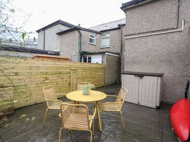 A patio with a yellow table and four chairs a wooden fence and a storage box at 5 Thomas Street Llanberis