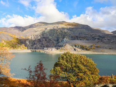 A body of water with trees in front and a mountain with a quarry and buildings at 5 Thomas Street in Llanberis